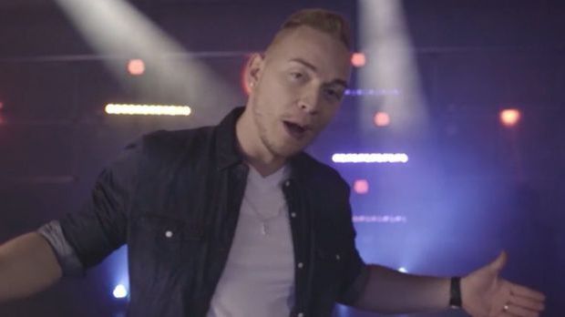 Erwin sieht mit geöffneten Armen in die Kamera und singt
