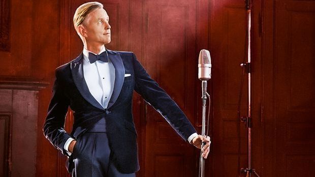 Max Raabe steht im Anzug lässig da, mit einem altmodischen Mikrofon in der li...